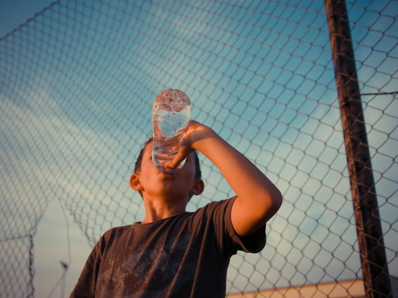 Un joven bebe agua en una botella de plástico