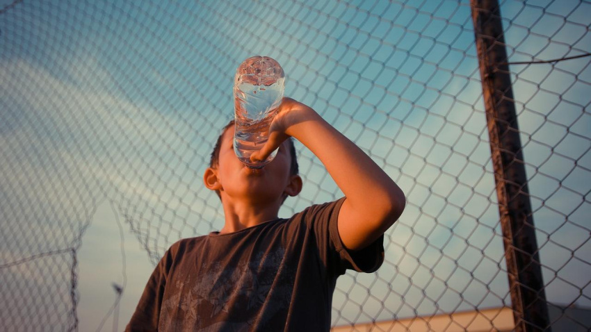 Un joven bebe agua en una botella de plástico