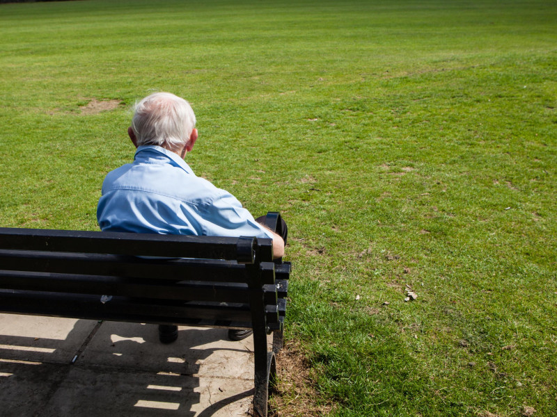 Un hombre anciano en un banco mirando hacia el parque