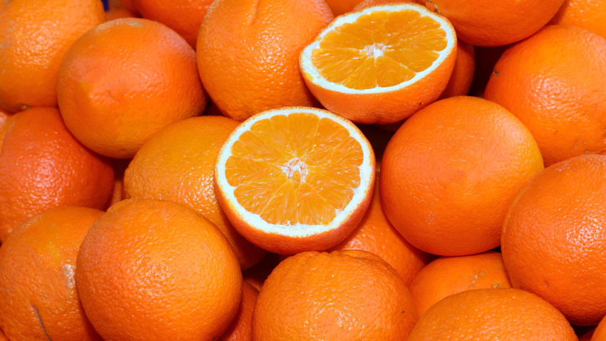 Fondo de muchas naranjas maduras y algunas cortadas por la mitad para la venta en la frutería