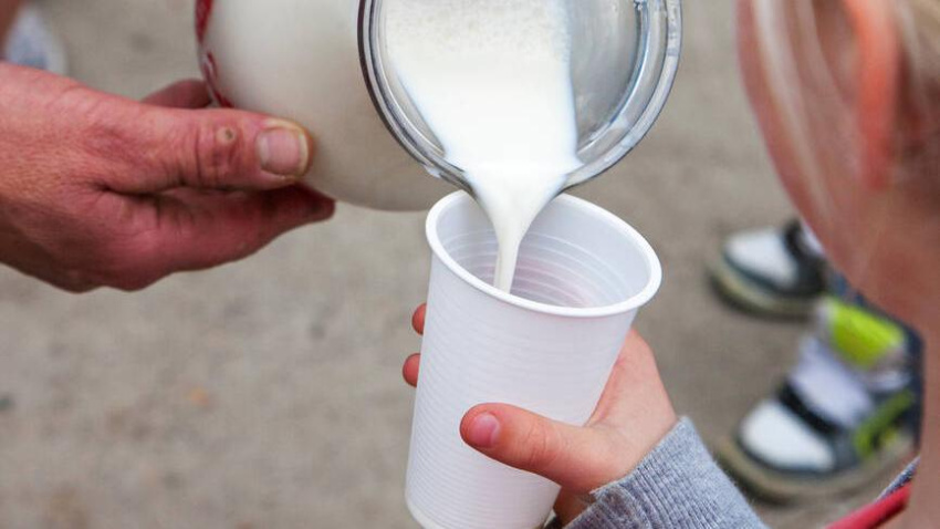 Una niña sujeta un vaso de plástico mientras le sirven un poco de leche