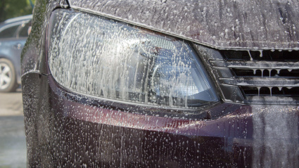 Un conductor limpia los faros de su vehículo con agua y jabón