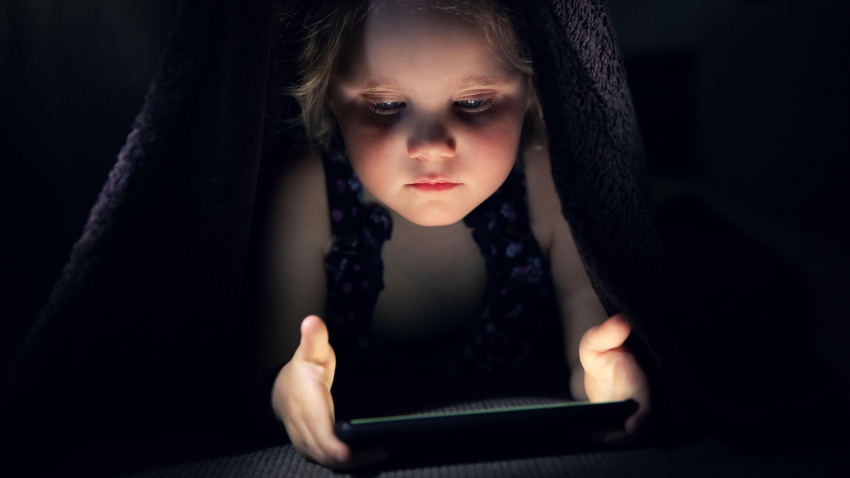 Una niña utilizando un teléfono móvil en la cama antes de dormir