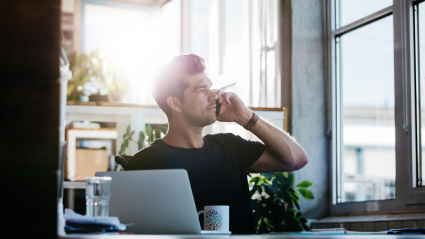 Un chico joven hablando por teléfono desde el escritorio de su casa