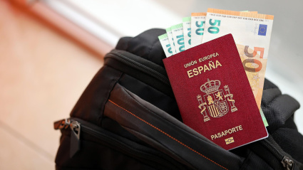 Un pasaporte español con billetes sobre una mochila
