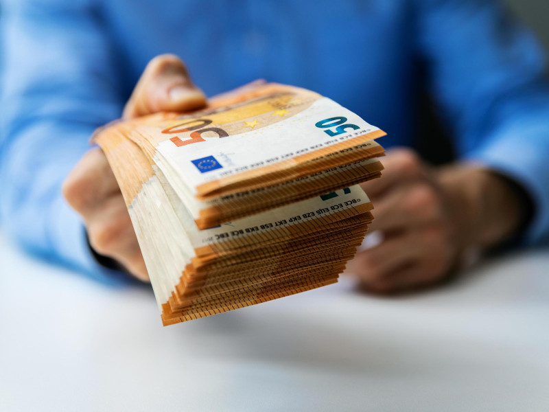 Un hombre tiende su mano llena de billetes para entregar el dinero