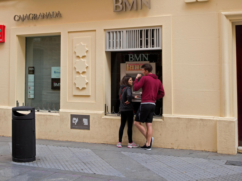 Un hombre y una mujer utilizan el cajero automático del Banco BMN en Cádiz