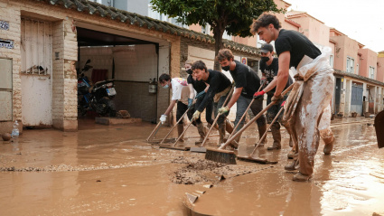 Grupo de voluntarios barre el lodo y el agua sucia de las calles hacia las alcantarillas durante las inundaciones de la dana. Alfafar