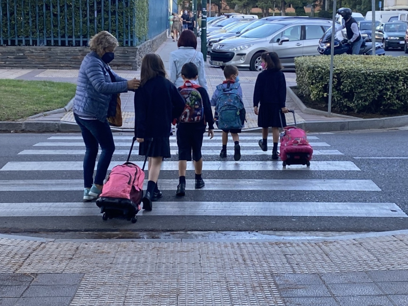 Varios alumnos con sus padres cruzan por un paso de peatones para acudir al colegio