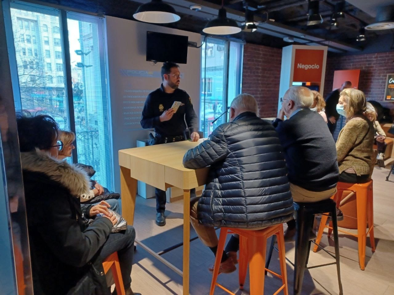 Un agente instruye a personas mayores en el uso seguro de móviles en la tienda de Orange