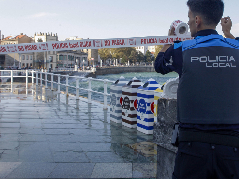 Un agente de la Policía Local de Gijón cierra un tramo del paseo del Muro de San Lorenzo