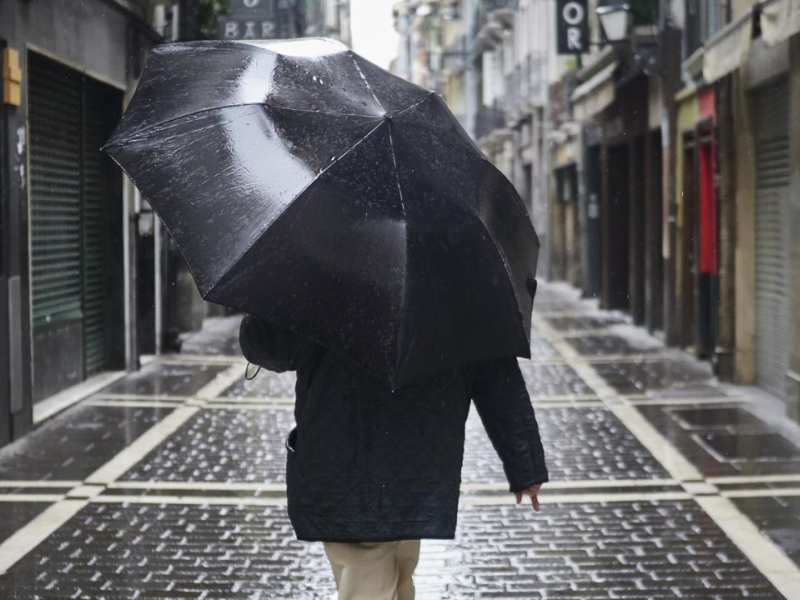 Una persona camina protegiéndose con un paraguas por la lluvia por el casco viejo de Pamplona