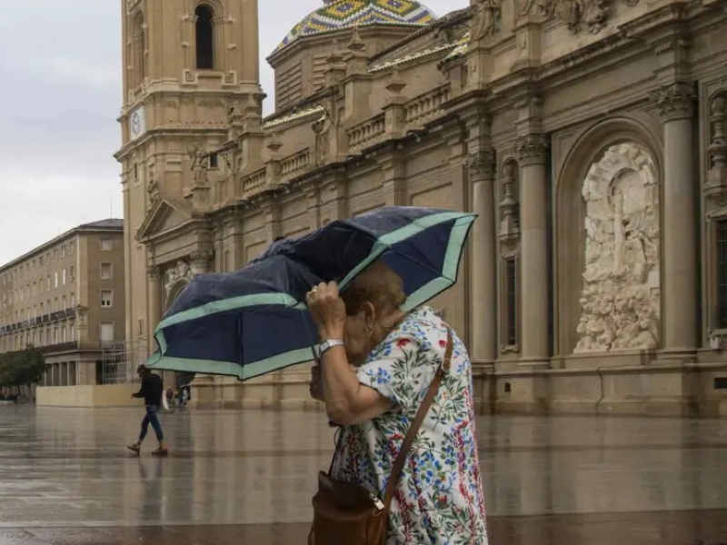 Imagen de archivo de una mujer cruzando la plaza del Pilar bajo la lluvia.