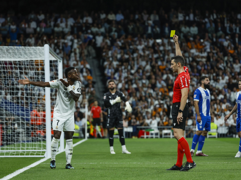 MADRID, 24/09/2024.- El colegiado Alejandro Muñiz Ruiz (d) muestra tarjeta amarilla al delantero del Real Madrid Vinícius Jr (i) durante el encuentro de la séptima jornada de LaLiga que Real Madrid y Deportivo Alavés disputan hoy martes en el estadio Santiago Bernabéu. EFE/Juanjo Martín