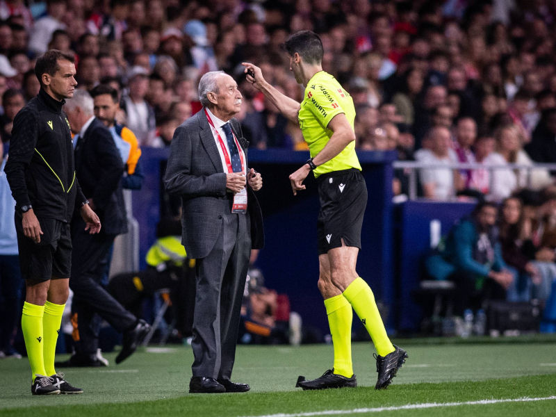 El colegiado del derbi madrileño habla con el delegado de campo del Atlético de Madrid.