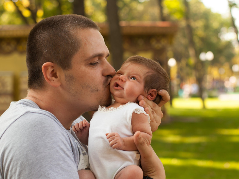 Padre sosteniendo y besando a una niña recién nacida