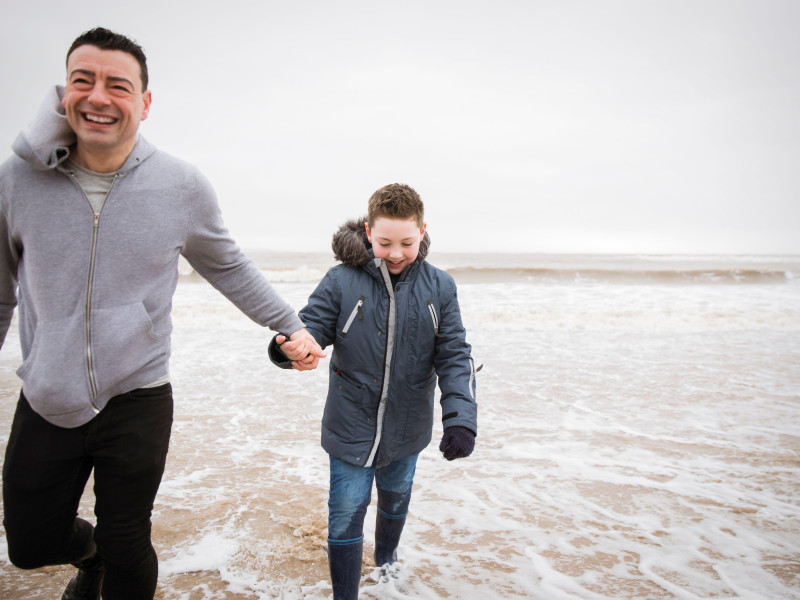 Padre e hijo felices vadeando las olas del océano en invierno