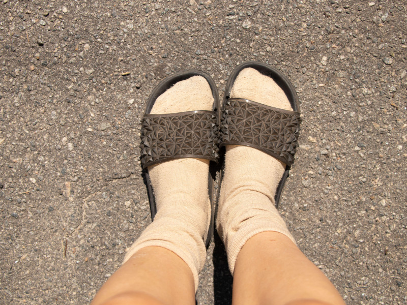 Pies femeninos en calcetines y chanclas sobre asfalto gris