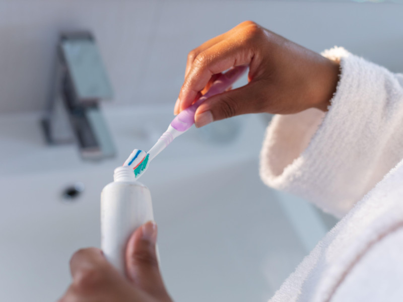 Sección media de la colocación de pasta de dientes en el cepillo de dientes en el baño