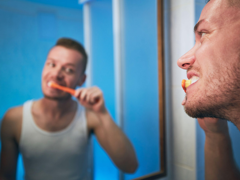 Rutina de higiene matutina. Hombre cepillándose los dientes y mirándose en el espejo del baño de su casa.