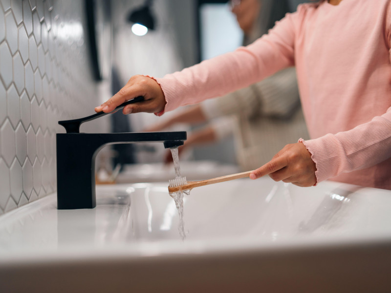 Primer plano de niña con cepillo de dientes ecológico en el baño, concepto de rutina matutina.