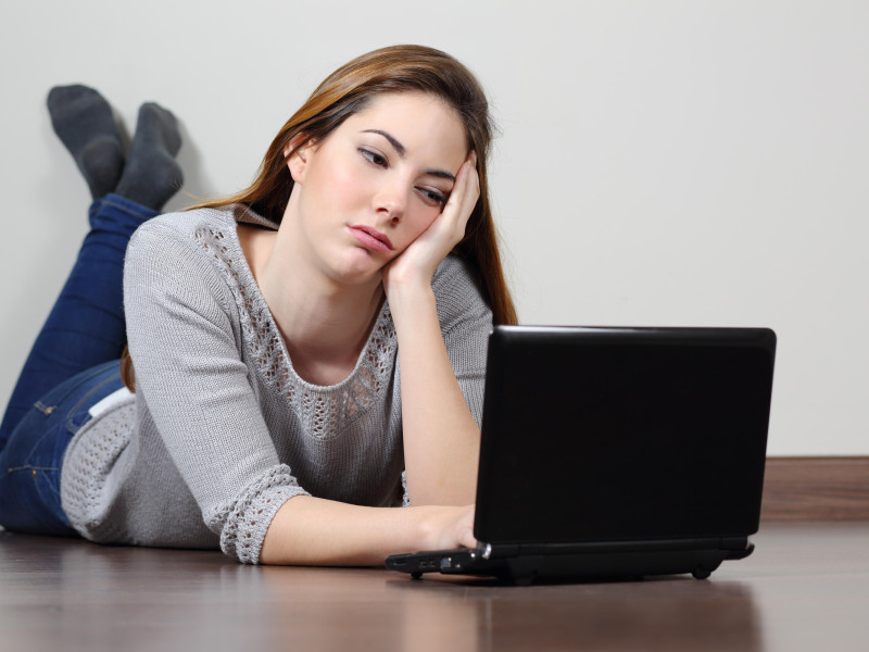 Chica adolescente aburrida navegando en las redes sociales en una computadora portátil tirada en el suelo en casa