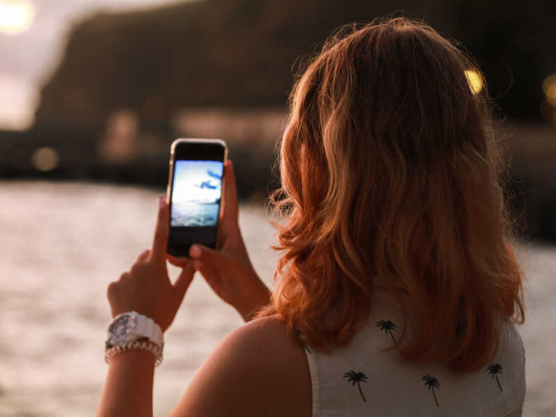 Una adolescente pelirroja toma una foto con su teléfono móvil en la costa del mar al atardecer