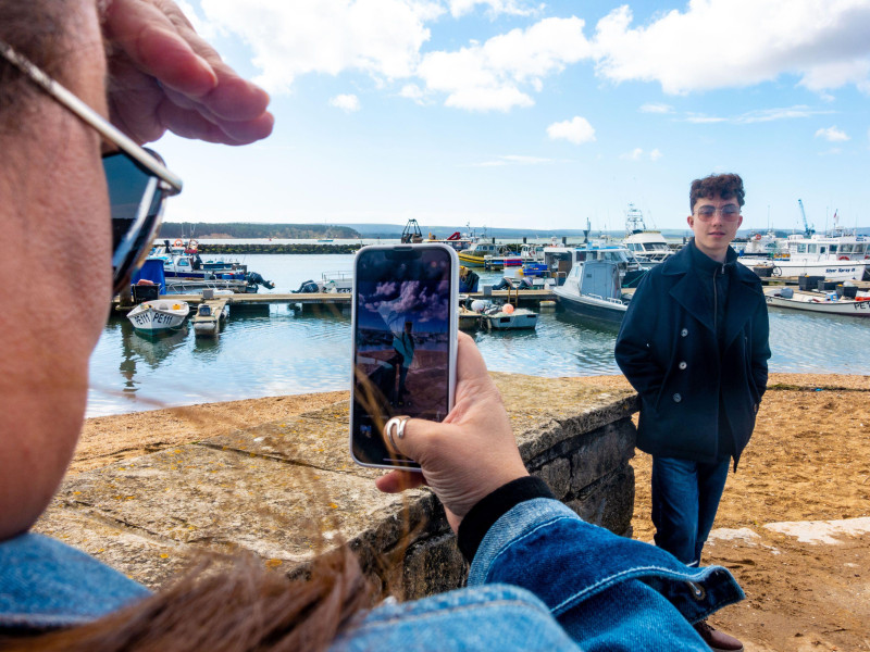 Una madre toma una foto de su hijo adolescente que pide la fotografía en su teléfono móvil.