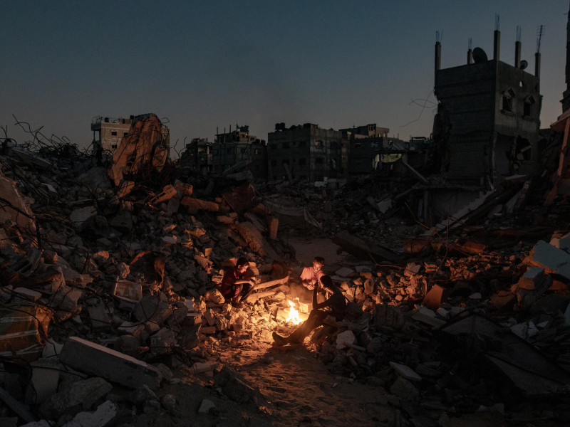 Palestinos sentados junto a un fuego sobre los escombros de su casa destruida en Khan Yunis, en el sur de la Franja de Gaza, el 20 de octubre de 2024