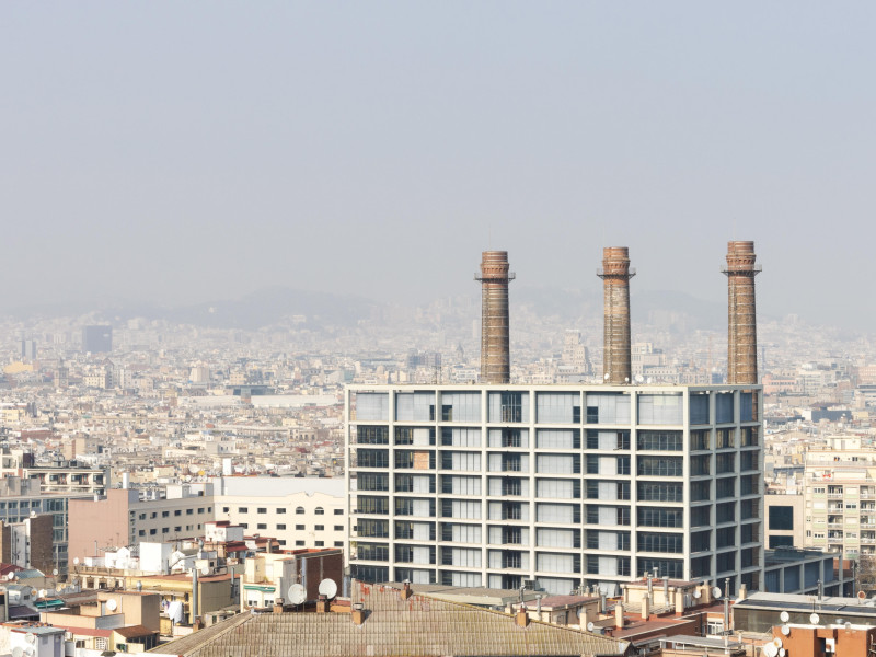 Imagen de la ciudad de Barcelona con aire contaminado. Edificio industrial con chimeneas en primer plano