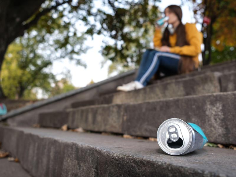 Una lata de aluminio exprimida y un adolescente que bebe bebida energética sentado en las escaleras.