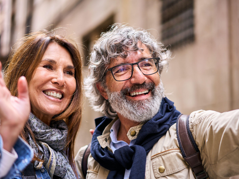 Primer plano de una feliz pareja heterosexual caucásica madura de pie juntos al aire libre saludando a un amigo