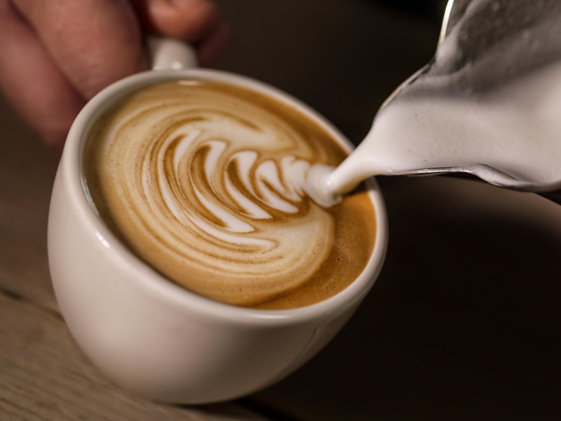 Mano de barista preparando café con leche o capuchino vertiendo leche haciendo arte latte