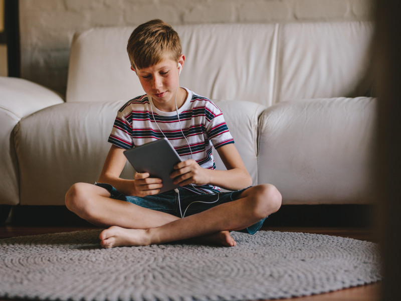 Niño sentado en el suelo con auriculares y jugando a videojuegos en una tableta digital. Niño con auriculares jugando a un juego en línea en una tableta en casa