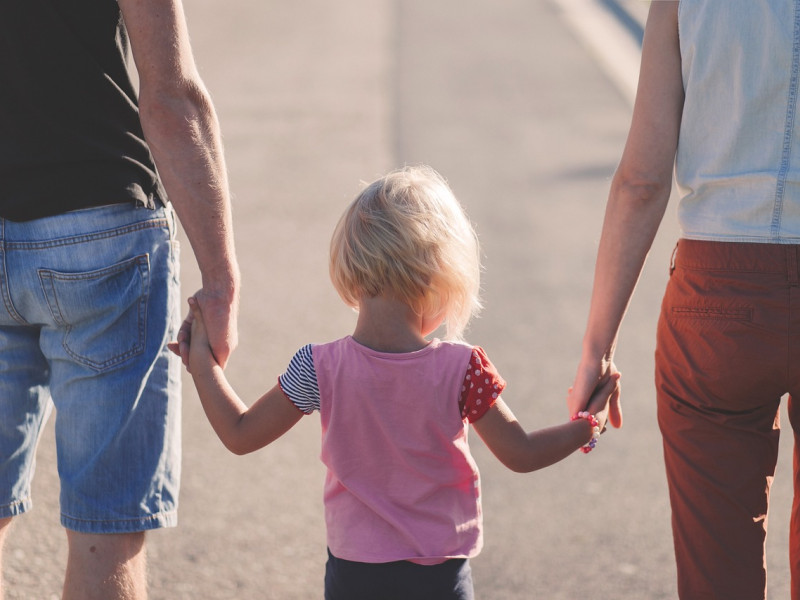 Una niña pasea de la mano de sus padres