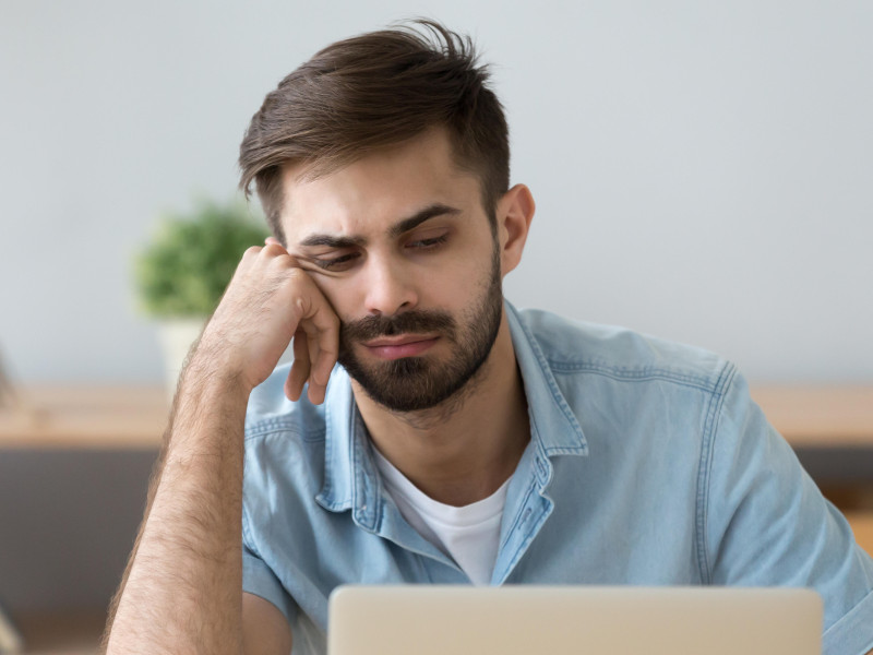 Un hombre perezoso se siente desmotivado al sentarse cerca de una computadora portátil en casa