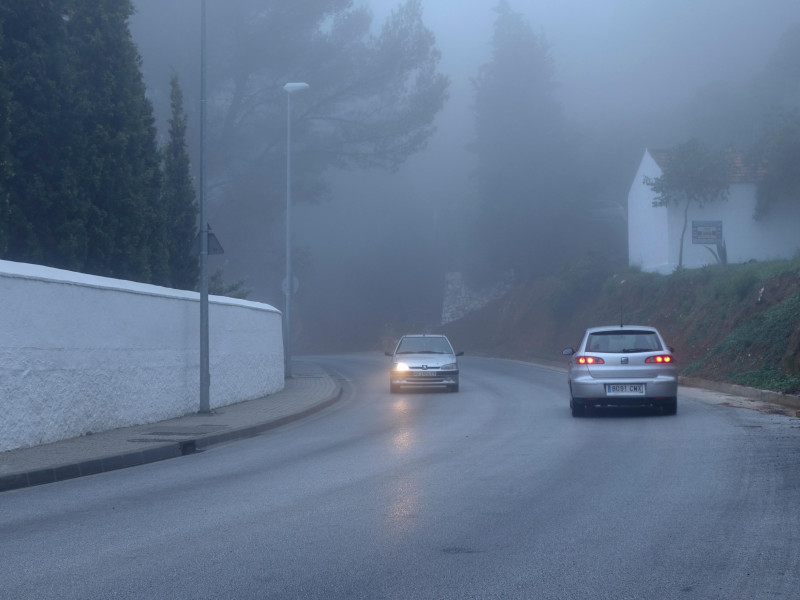 Dos coches circulando con niebla. Un coche con un faro averiado. Carretera de montaña con niebla. España.