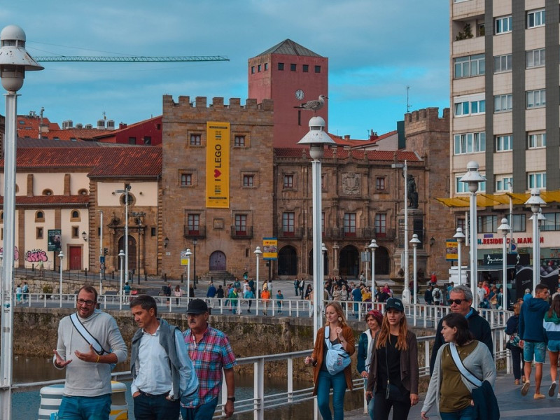 Gente paseando por los Jardines de la Reina, con Cimadevilla al fondo, en Gijón