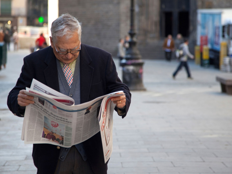 Un anciano lee el periódico en las calles del antiguo Barrio Gótico de Barcelona, ​​España