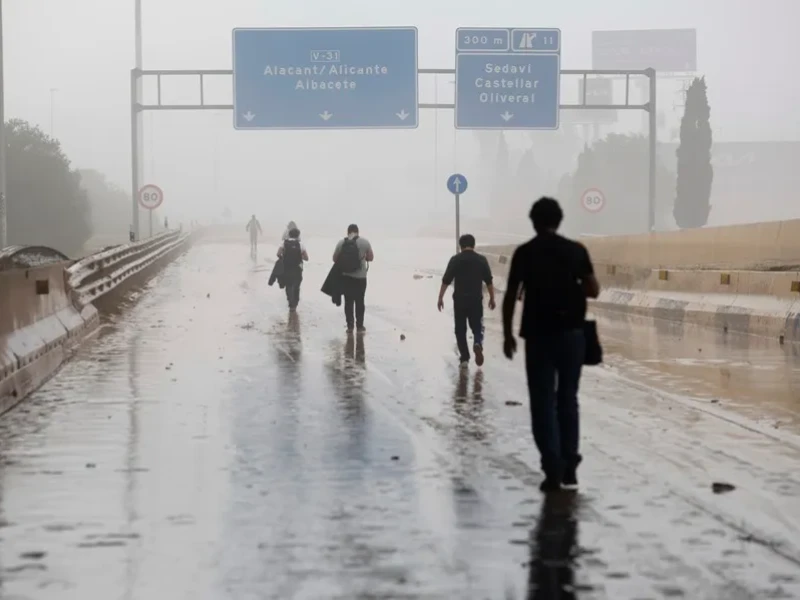 Varias personas transitan por la V-31 cerrada al tráfico a causa de las lluvias torrenciales