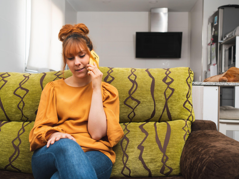 Mujer caucásica sentada en un sofá hablando por teléfono