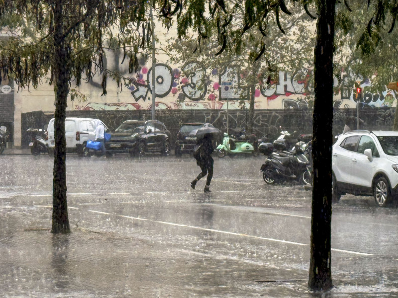 Una persona camina bajo la lluvia en Barcelona este miércoles cuando la Generalitat ha lanzado un aviso de tiempo violento en la corona de Barcelona, en concreto en las comarcas del Baix Llobregat, el Garraf, el Barcelonès, el Vallès Occidental y el Alt Penedès, ante la previsión de rachas de viento de más de 90 kilómetros por hora y granizo de más de dos centímetros de diámetro