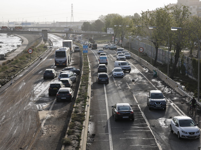 Varios coches circulan entre los vehículos afectados por la dana en la V30 a la altura de La Torre este viernes en Valencia. Los servicios de emergencia siguen trabajando en tareas de desescombro tras la devastadora dana que ha dejado al menos 95 fallecidos y que continuará en algunas zonas. EFE/ Biel Alino