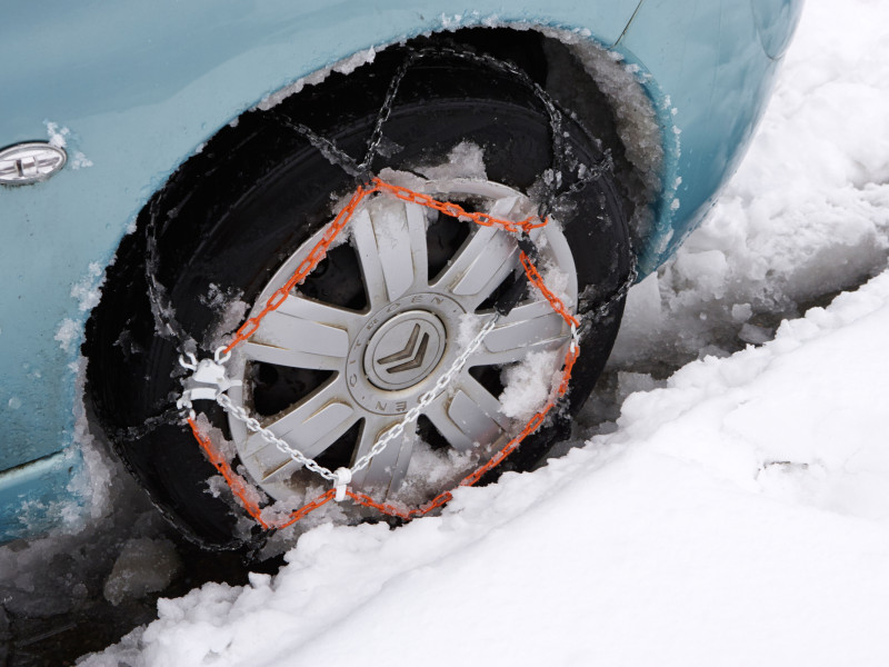 Vehículo de carretera con cadenas de nieve instaladas en el automóvil durante una fuerte tormenta de nieve invernal