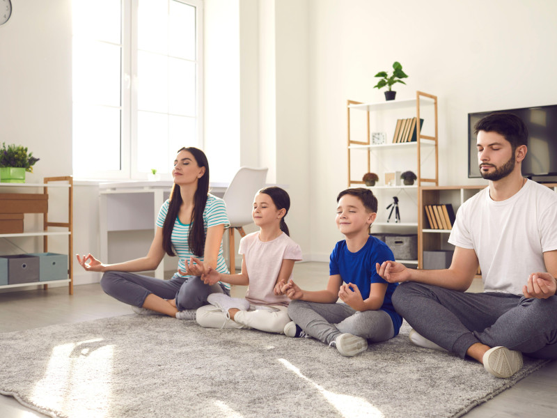 Familia joven feliz con niños pequeños haciendo yoga y practicando meditación juntos