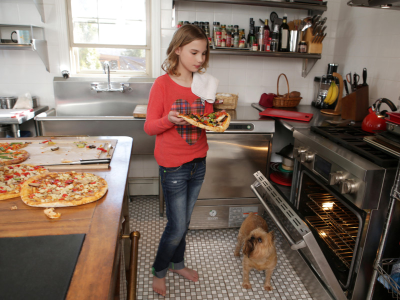 Chica joven en la cocina, poniendo pizza en el horno