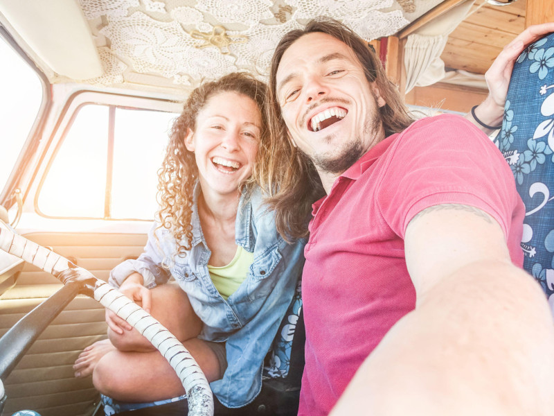 Feliz pareja dentro de una minivan para un viaje por carretera: personas adultas tomándose selfies en vacaciones de verano viajando alrededor del mundo