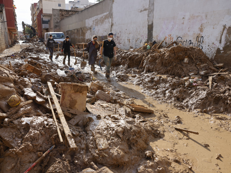 Voluntarios pasan ante los escombros acumulados a los lados de una calle de Masanasa