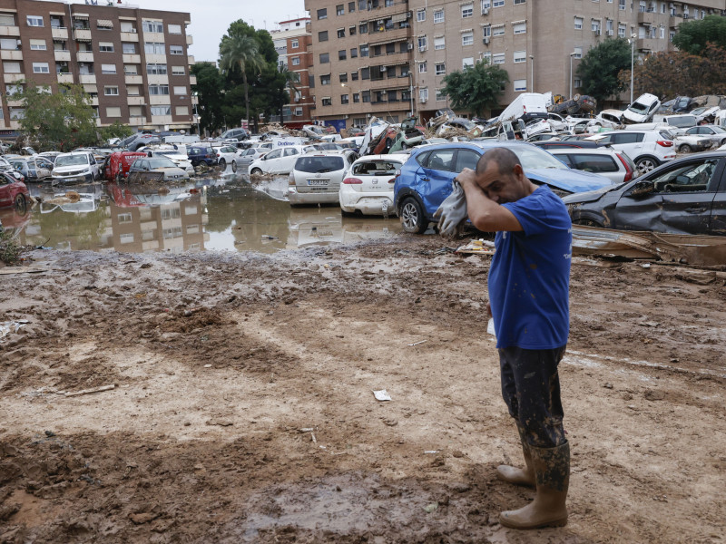 Un hombre junto a varios coches, arrastrados por el agua tras el paso de la dana, en Paiporta