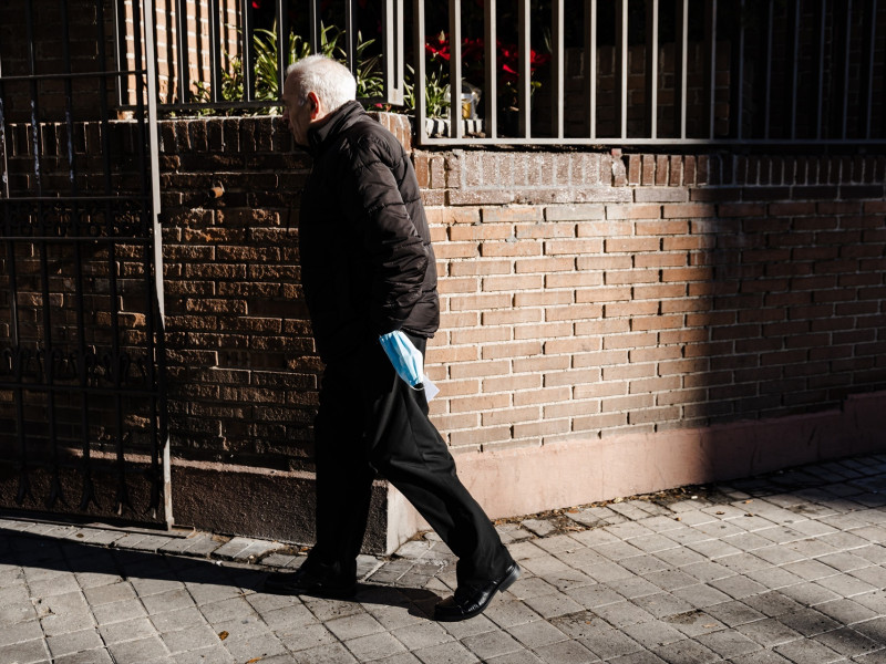 Un hombre con una mascarilla en la mano por una calle de Madrid